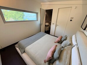Une chambre avec un grand lit, une fenêtre donnant sur un beau paysage et une porte menant à la salle de bain.