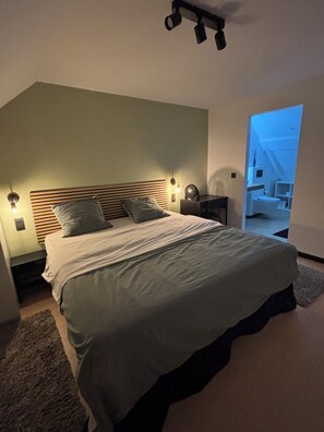 Quarto moderno com uma cama grande, luminárias de cabeceira e vista para um banheiro.