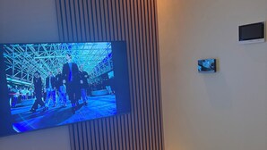 Een moderne woonkamer met een grote flatscreen televisie aan een wand met verticale latten, een witte entertainmentkast eronder en een klein secundair scherm op de muur.