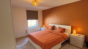 Een slaapkamer met een bed, nachtkastjes, een raam met zonwering en een plafondlamp.
