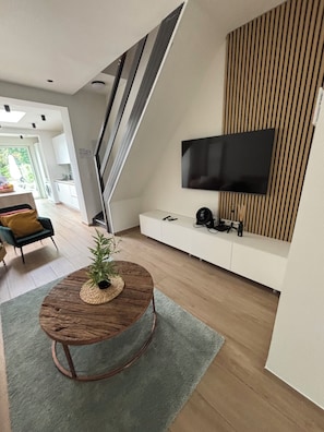 A modern living room with a wooden coffee table, a flat-screen TV mounted on a wall, and a staircase leading to another level. - Family home with a garden. Brussels is a 9-minute train ride away. Near Hallerbos (Halle)