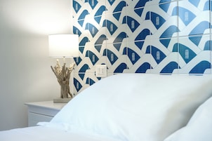 Una camera da letto con un letto, un comodino, una lampada e una parete con motivo geometrico.