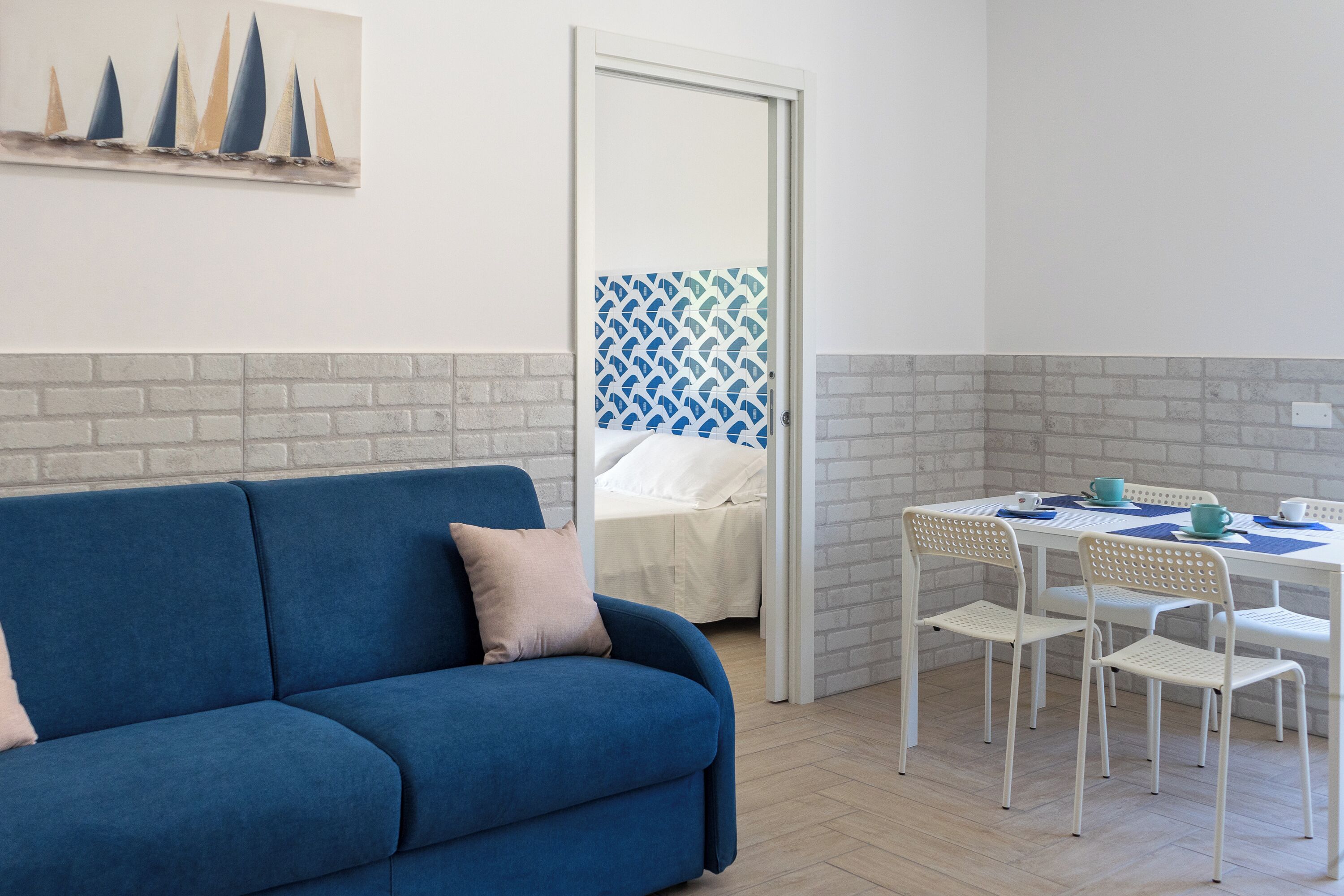 Ein Zimmer mit einem blauen Sofa, einem Esstisch mit Stühlen und einem Bett mit einer gemusterten Wand.