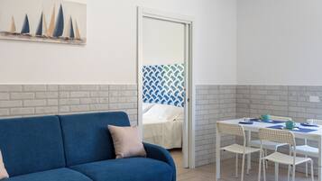 Una habitación con un sofá azul, una mesa de comedor con sillas y una cama frente a una pared estampada.
