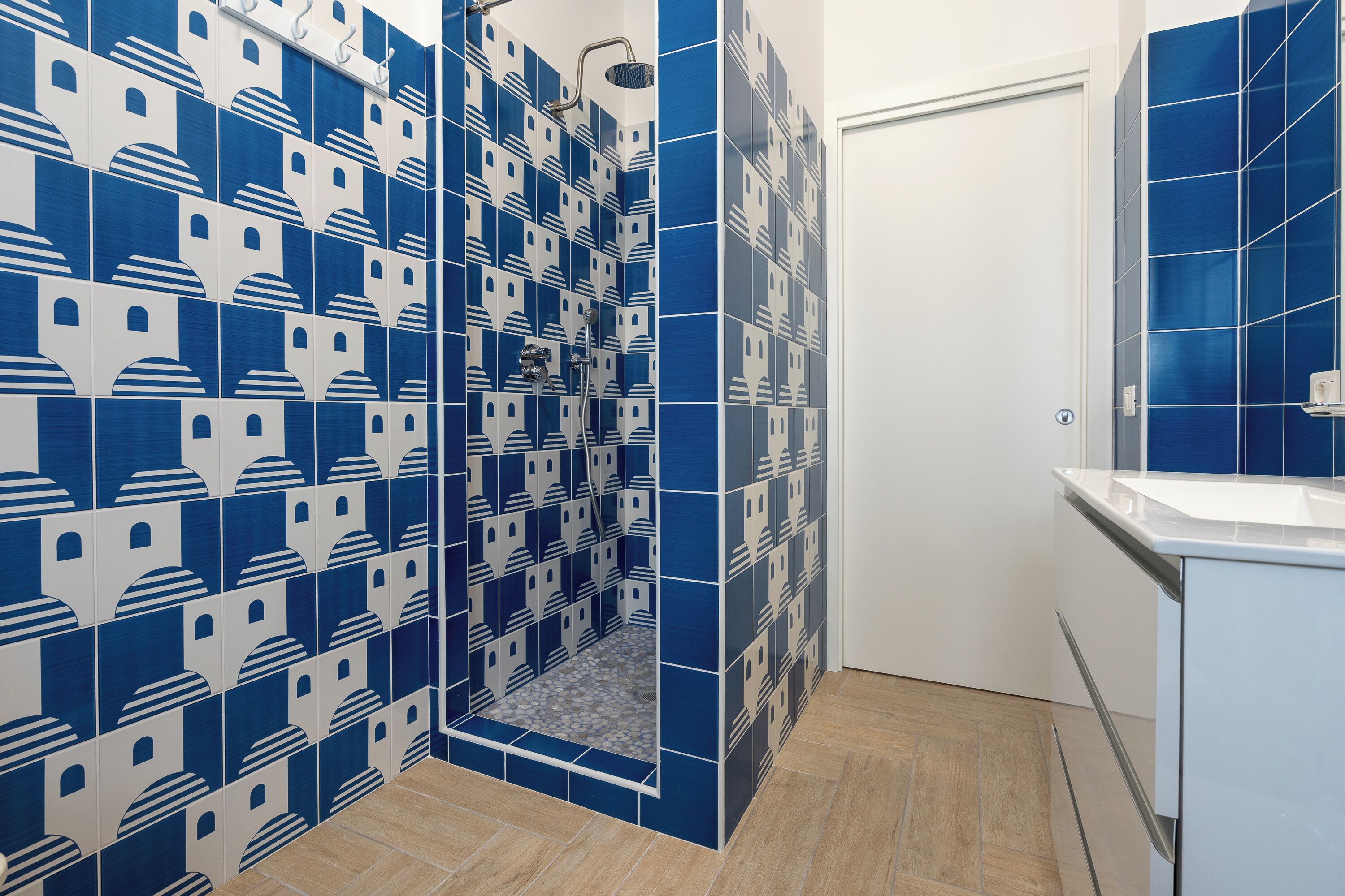 A bathroom with blue and white patterned tiles, a shower area, and a white sink with a mirror.