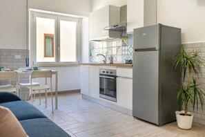 A compact kitchen with a built-in oven, a stainless steel refrigerator, and a window with a view of the outside. - Casa Canzatora (Sperlonga)