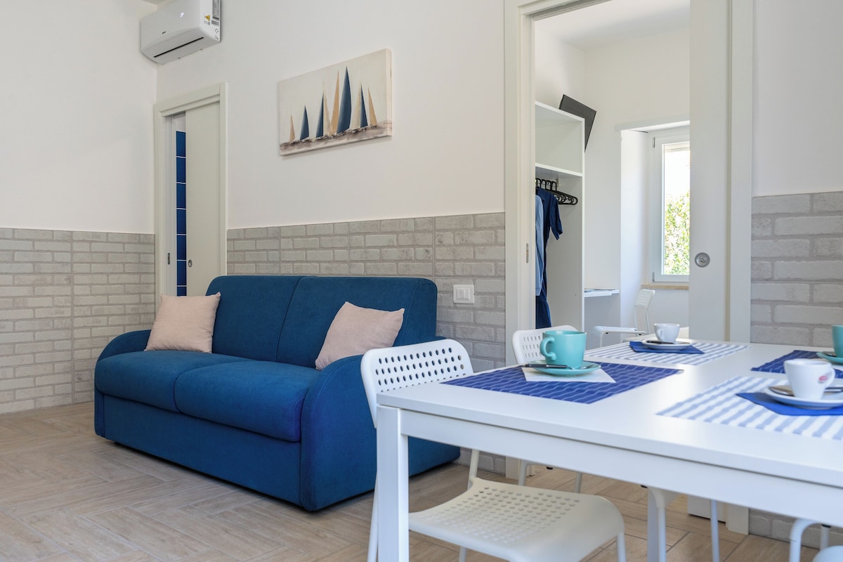 A modern room with a blue sofa, a white table with blue placemats, and a painting on the wall.