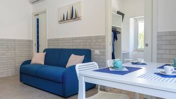 A modern room with a blue sofa, a white table with blue placemats, and a painting on the wall.