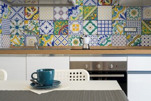 Una cocina con salpicadero de azulejos, una cafetera y una mesa con una taza azul.