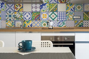 Una cucina con pareti rivestite di piastrelle, una macchina da caffè e un tavolo con una tazza blu.