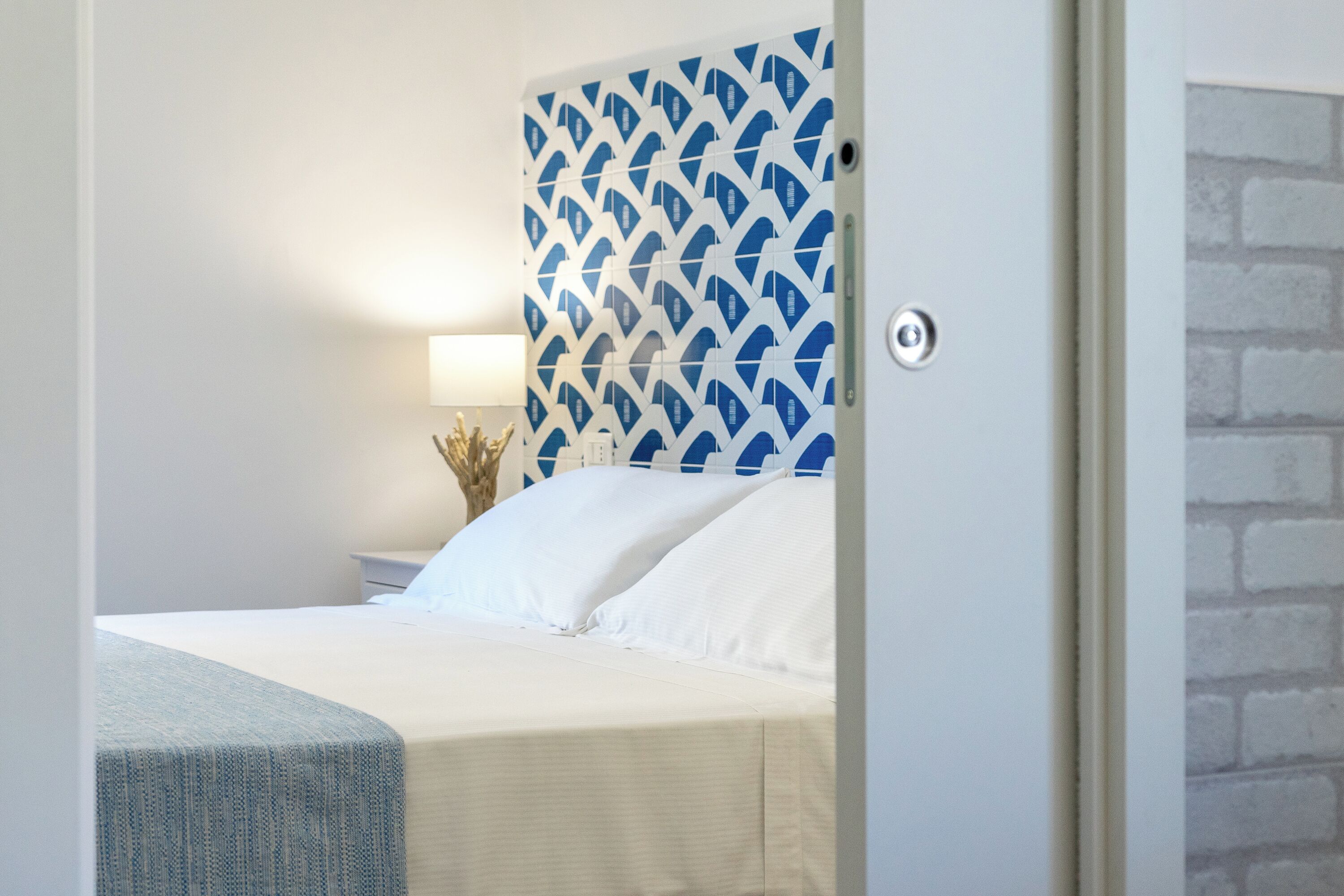 Une chambre à coucher avec un lit, une table de chevet, une lampe et un mur décoré d’un motif.