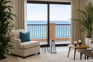 Una habitación con sofá, una mesita, una planta en maceta y vista al océano desde un balcón.
