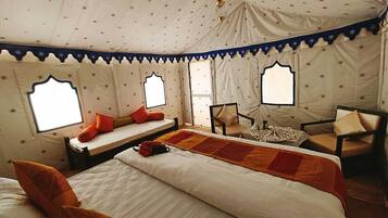 A room with a large bed, two smaller beds, a chair, a table, and a window with star-patterned curtains.