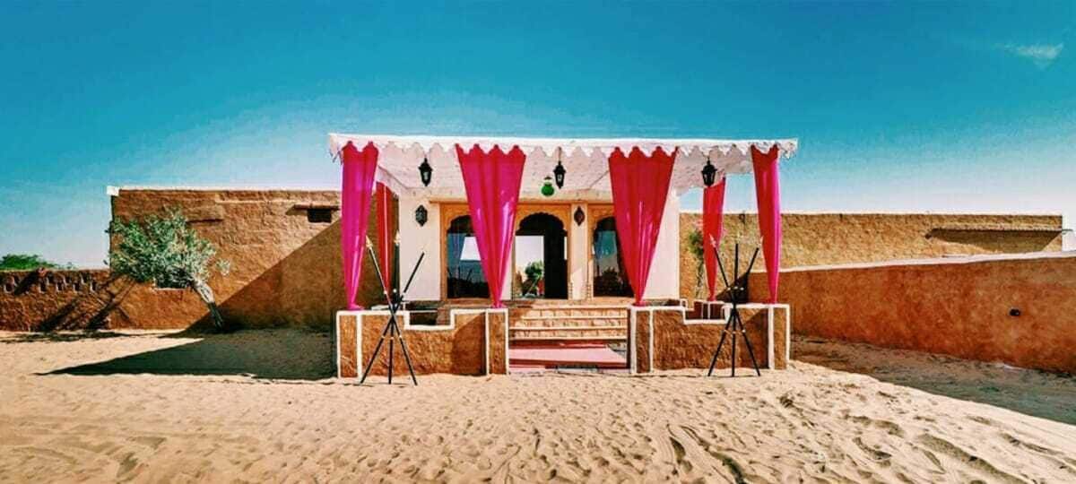A building with a covered outdoor area, a sandy ground, and a clear blue sky.