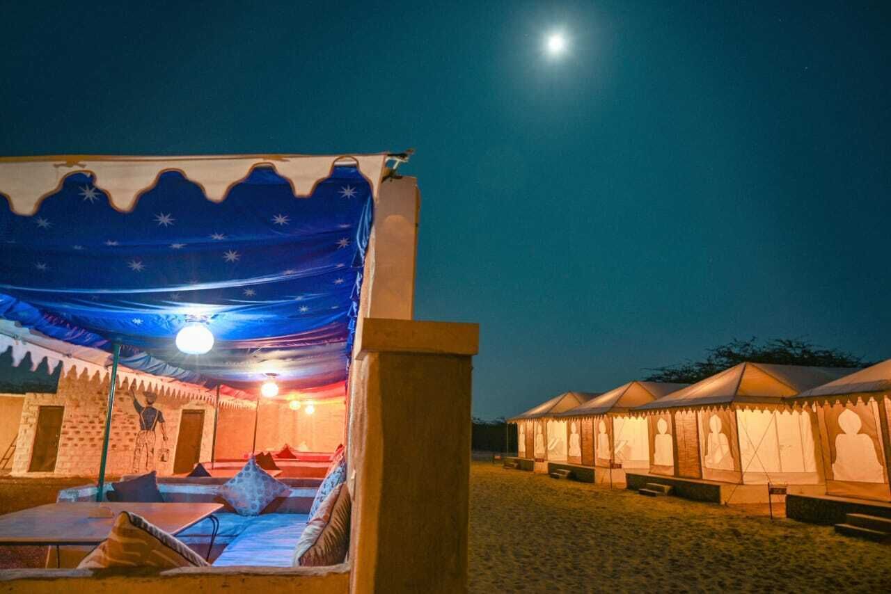 A tented accommodation with a bed, pillows, and a night sky view.