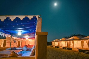 A tented accommodation with a bed, pillows, and a night sky view.