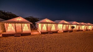 A row of tents with Buddha statues on the front, set on a sandy beach at night.