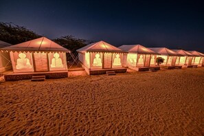 A row of tents with Buddha statues on the front, set on a sandy beach at night. - Explore Overnight Desert Camp (Jaisalmer)