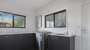 A modern kitchen with dark cabinets, a stainless steel refrigerator, and a window with a view of trees and a house. - Spacious Sandy Bay Retreat with Water Views (Sandy Bay)