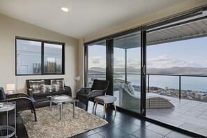 A modern living room with a sofa, chairs, a coffee table, and a view of the sea through large glass doors. - Oceanview Oasis - Close to CBD and Airport (Sandy Bay)