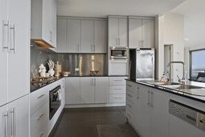 A modern kitchen with stainless steel appliances, grey cabinetry, and a black countertop. - Oceanview Oasis - Close to CBD and Airport (Sandy Bay)