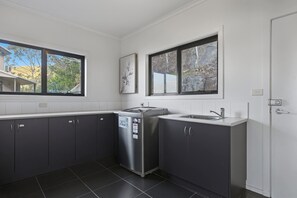 A modern kitchen with dark cabinets, a stainless steel refrigerator, and a window with a view of trees and a building. - Oceanview Oasis - Close to CBD and Airport (Sandy Bay)