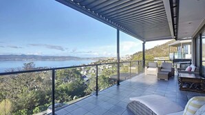A balcony with a view of a body of water and hills, furnished with a sofa and a dining table. - Spacious Sandy Bay Retreat with Water Views (Sandy Bay)