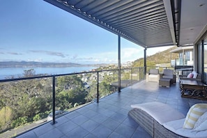 Ein Balkon mit Blick auf ein Gewässer und Hügel, ausgestattet mit einer Couch und einem Esstisch.