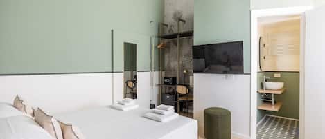 A bedroom with a bed, a mirror, a wardrobe, a small stool, and a bathroom with a sink and towel rack.