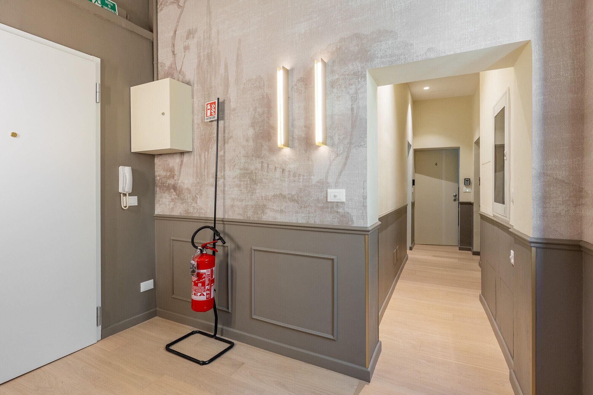A hallway with a fire extinguisher mounted on the wall, a phone, and a door with the number 4.