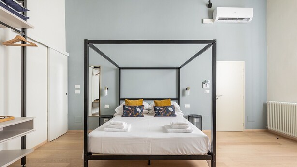 A four-poster bed with white linens and decorative pillows, a wardrobe with a mirror, and a radiator on the floor. - Suite Blue by Wonderful Italy (Bologna)