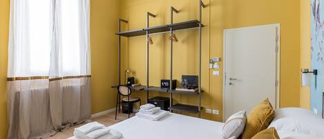Habitación de hotel con cama, escritorio con silla, armario y baño con cortina de ducha.