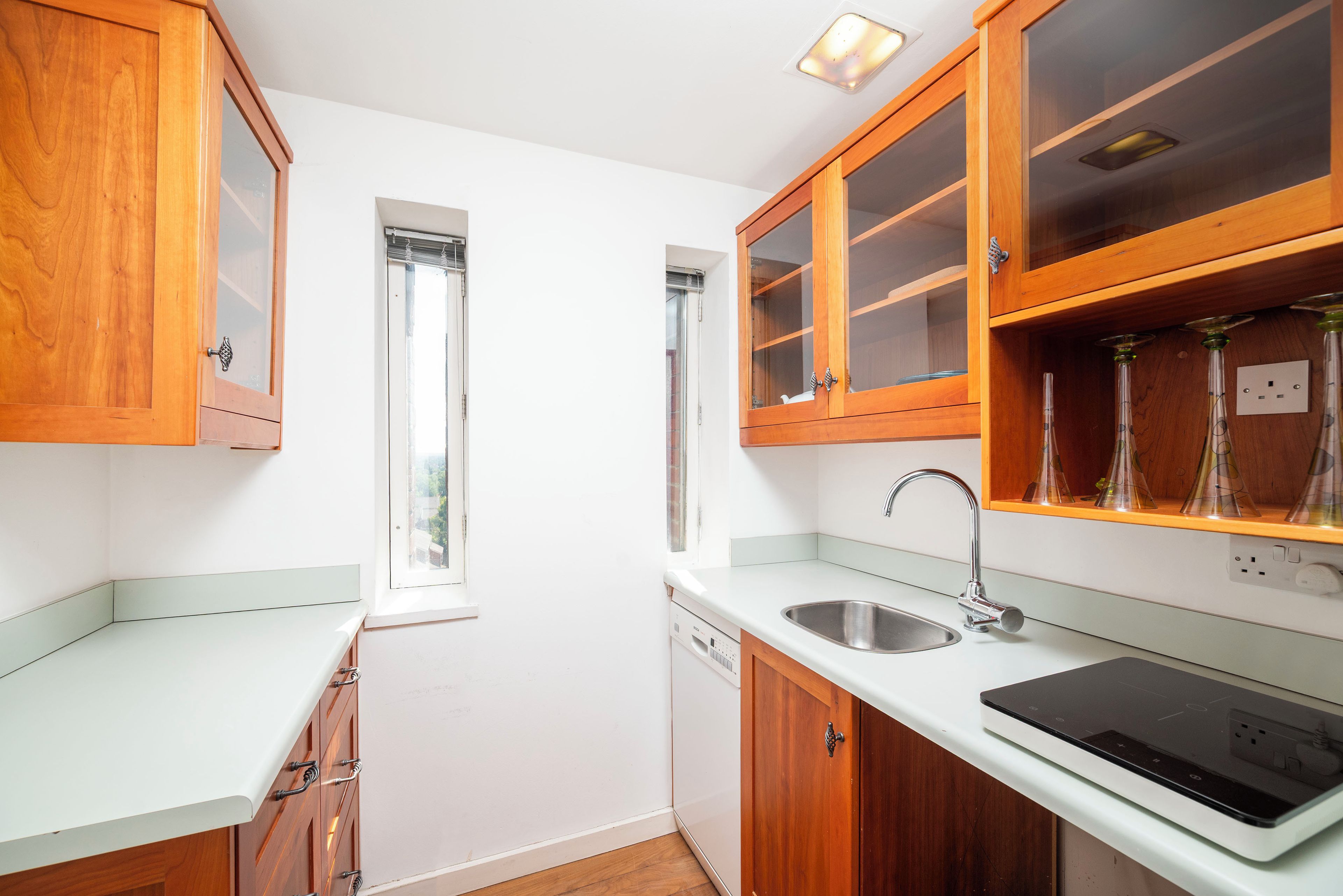 A compact kitchen with wooden cabinets, a built-in dishwasher, and a modern faucet.