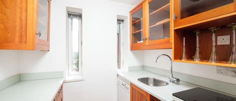 A compact kitchen with wooden cabinets, a built-in dishwasher, and a modern faucet.