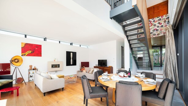 A modern living room with a dining area, a staircase, and a large window. - Historic 3BDR with Sky Lounge in Greenwich (Greater London)