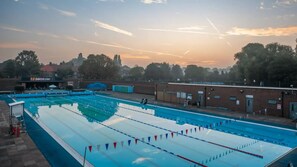 Ein Schwimmbecken mit Bahnen, einem Sprungturm und einem Gebäude im Hintergrund.