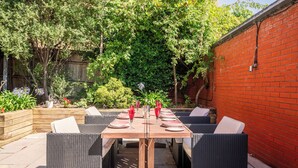 An outdoor patio with a wooden table set for dining, surrounded by wicker chairs. - Historic 3BDR with Sky Lounge in Greenwich (Greater London)