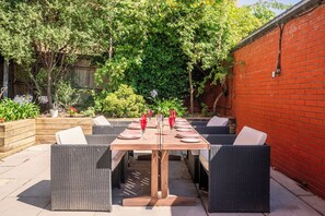 Eine Terrasse im Freien mit einem Holztisch, gedeckt für ein Essen, umgeben von Korbstühlen.