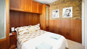 A bedroom with a bed, wooden wardrobe, two framed pictures on the wall, and a carpeted floor. - Historic 3BDR with Sky Lounge in Greenwich (Greater London)