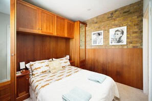 Ein Schlafzimmer mit einem Bett, einem Holzschrank, zwei gerahmten Bildern an der Wand und Teppichboden.
