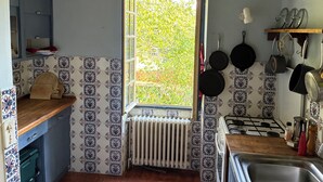Cocina con ventana, salpicadero de azulejos, encimera de madera y ollas colgantes.