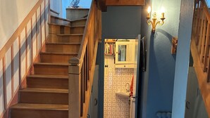 Una escalera de madera lleva a una zona de cocina con piso de baldosas, un lavamanos y un gabinete con espejo.