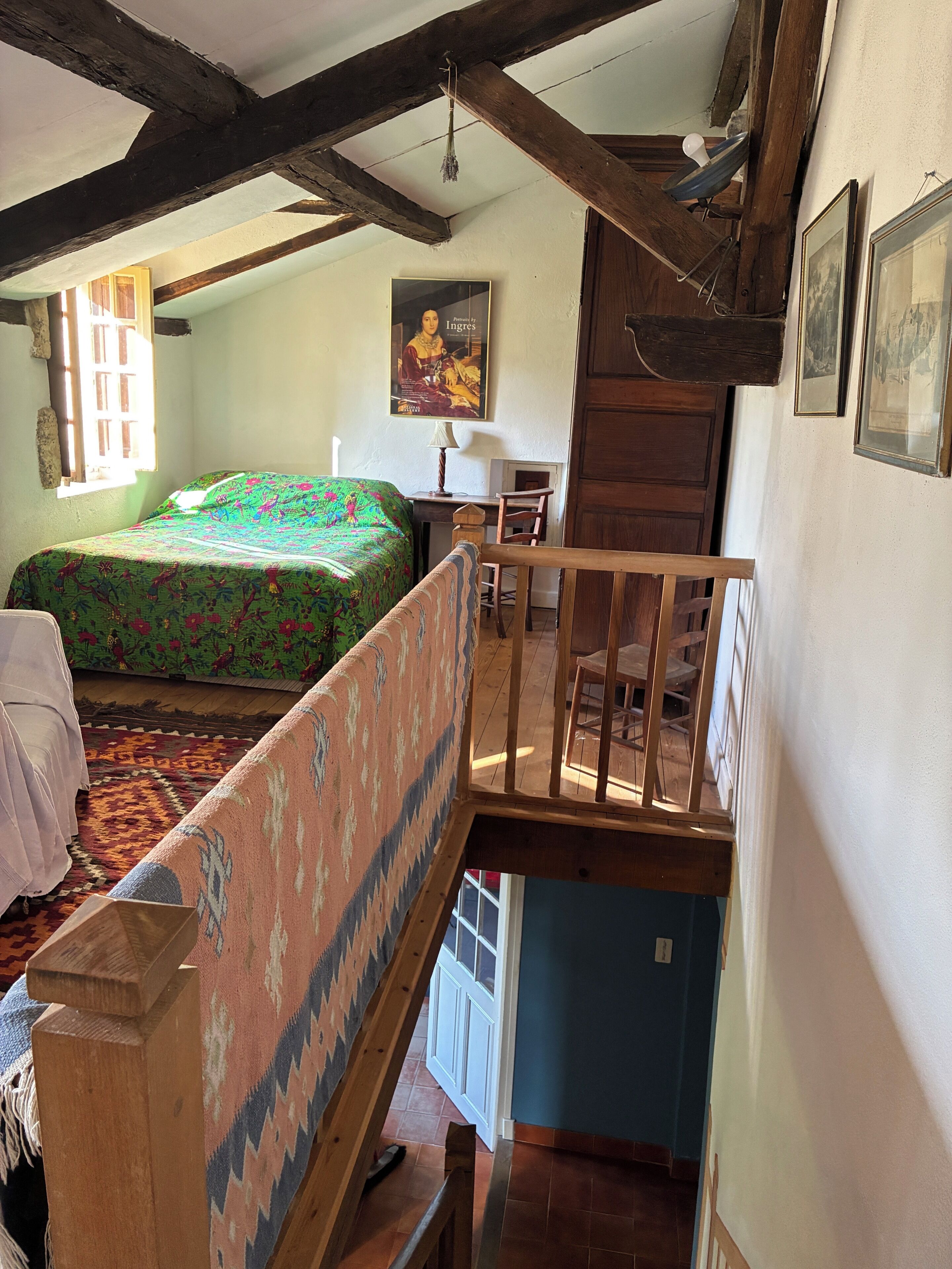 A room with a bed, a desk, a chair, and a staircase.