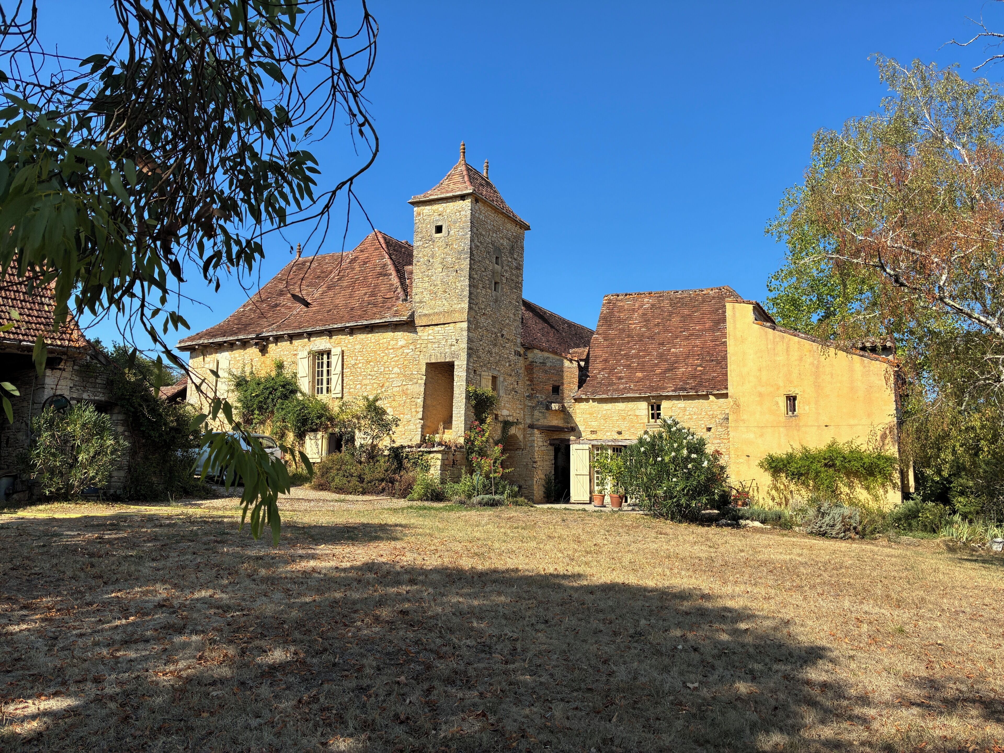A stone building with a tower, surrounded by dry grass and trees.