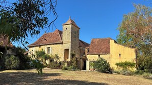 Un edificio de piedra con una torre, rodeado de pastizales secos y árboles.