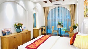 A hotel room with a bed, a desk, two chairs, a small table with a vase, and a window with curtains. - La Mandarina Hotel & Travel (Hanoi)