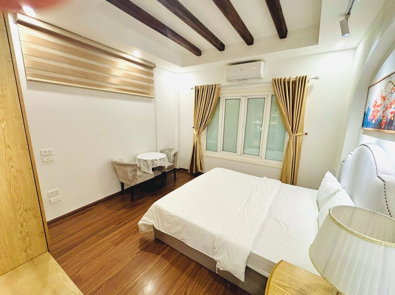 A hotel room with a bed, a small table, a chair, and a window with curtains.