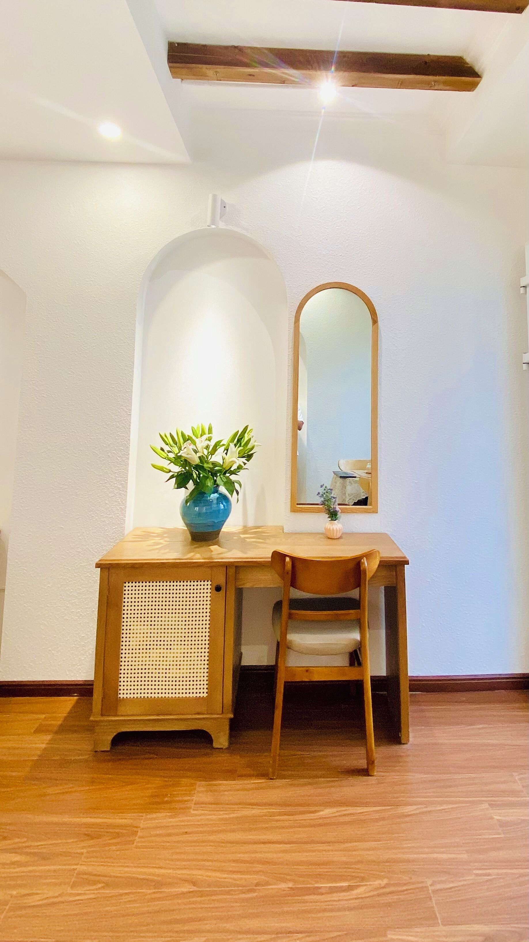 A wooden desk with a blue vase and a chair in a room with white walls and a wooden beam ceiling.