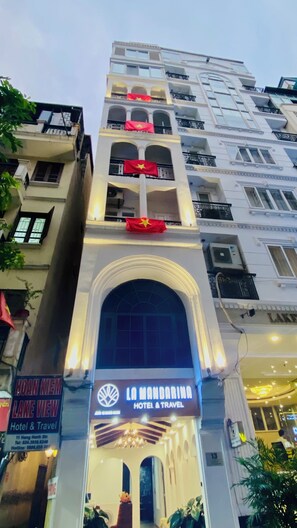 A hotel with a prominent entrance, multiple balconies, and flags. - La Mandarina Hotel & Travel (Hanoi)