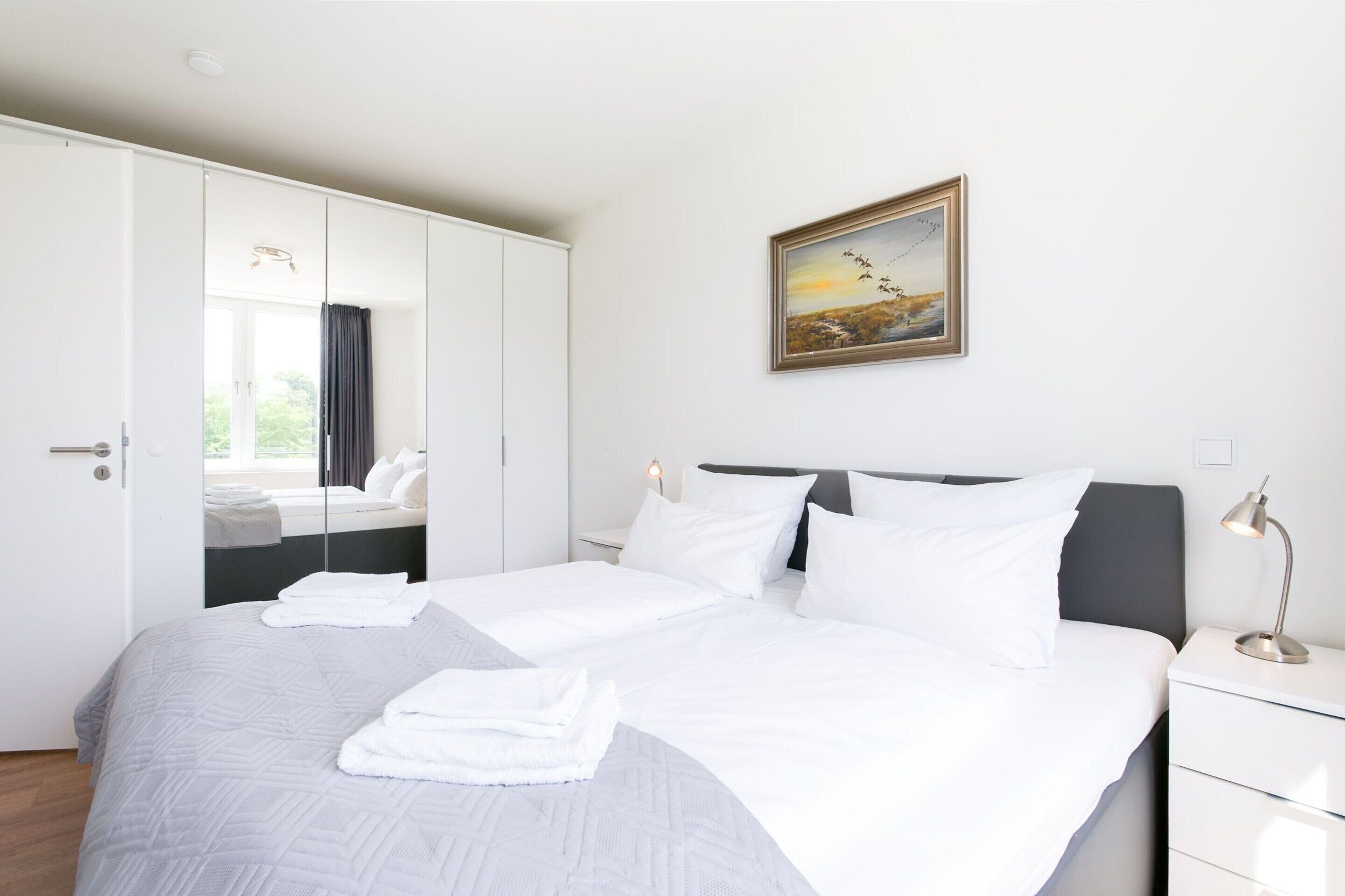 A hotel room with a bed, a wardrobe, a painting, and a nightstand.